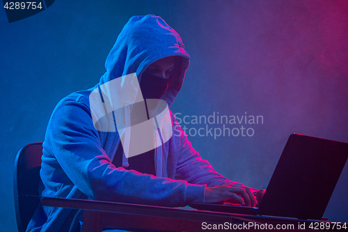 Image of Hooded computer hacker stealing information with laptop