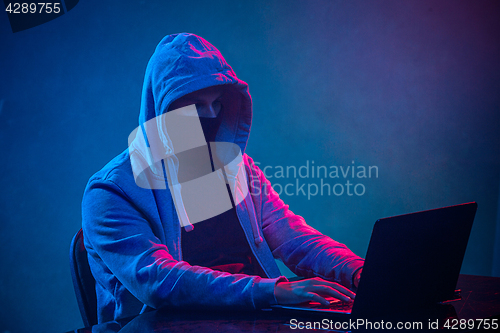 Image of Hooded computer hacker stealing information with laptop