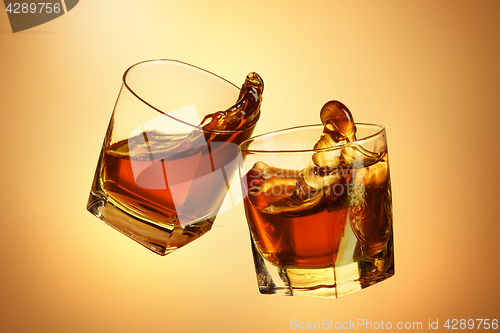 Image of Two whiskey glasses clinking together on brown