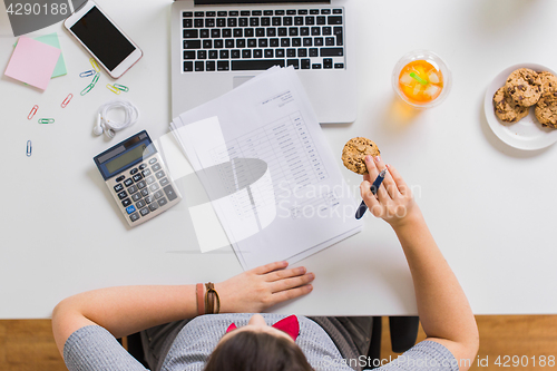 Image of woman with tax report eating cookie at office