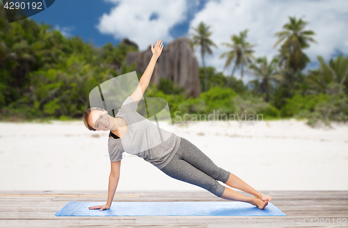 Image of woman doing yoga in side plank pose on beach