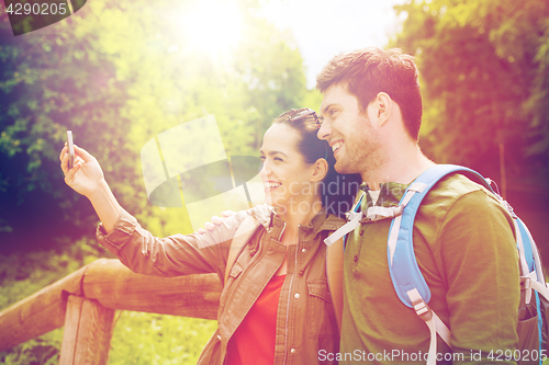 Image of couple with backpacks taking selfie by smartphone