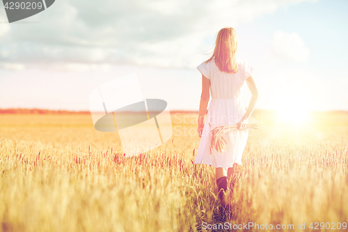 Image of young woman with cereal spikelets walking on field