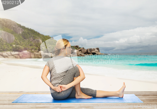 Image of woman doing yoga in twist pose on beach
