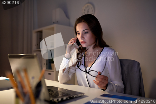 Image of woman with laptop calling on smartphone at office