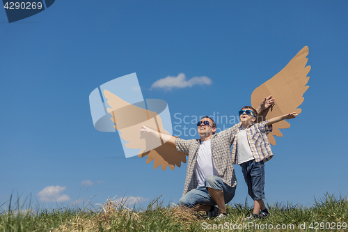 Image of Father and son playing with cardboard toy wings in the park at t