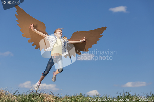 Image of Little girl playing with cardboard toy wings in the park at the 