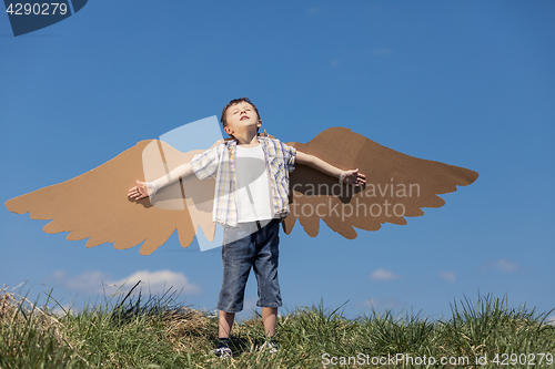 Image of Little boy playing with cardboard toy wings in the park at the d