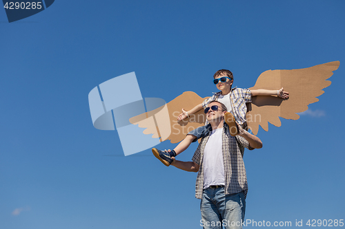 Image of Father and son playing with cardboard toy wings in the park at t