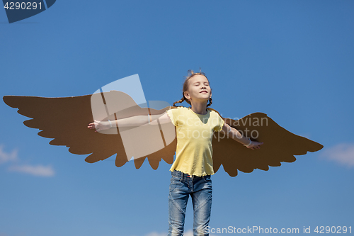 Image of Little girl playing with cardboard toy wings in the park at the 