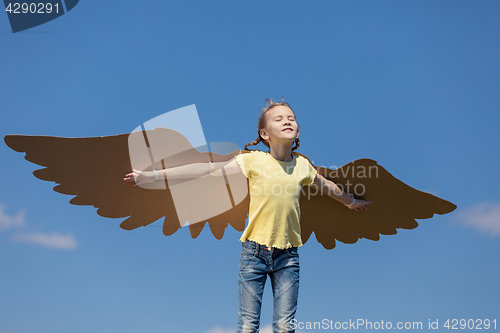 Image of Little girl playing with cardboard toy wings in the park at the 