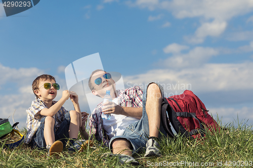 Image of Father and son sitting in the field at the day time.