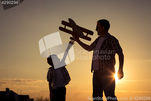 Image of Father and son playing with cardboard toy airplane in the park a