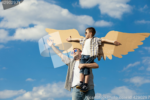 Image of Father and son playing with cardboard toy wings in the park at t