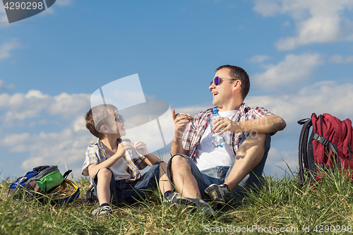 Image of Father and son sitting in the field at the day time.