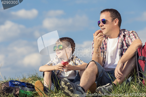 Image of Father and son sitting in the field at the day time.