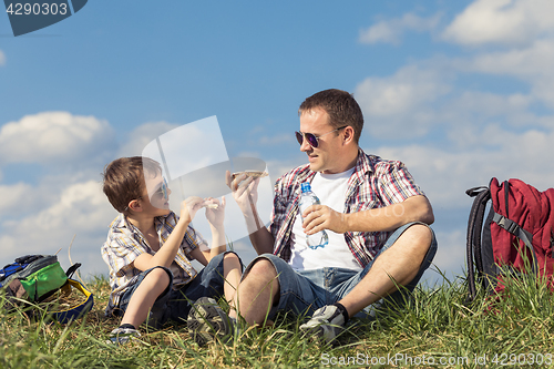 Image of Father and son sitting in the field at the day time.