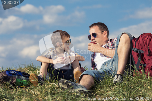 Image of Father and son sitting in the field at the day time.