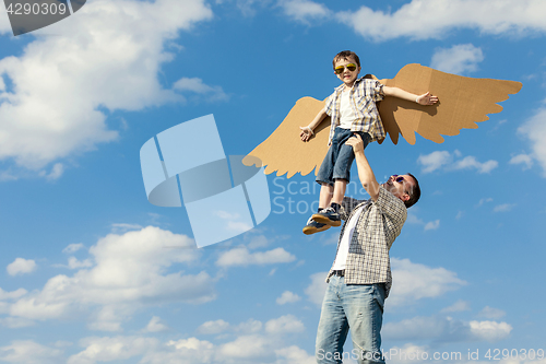 Image of Father and son playing with cardboard toy wings in the park at t