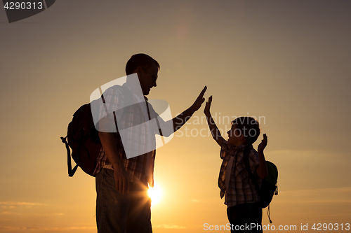 Image of Father and son walking on the field at the sunset time.