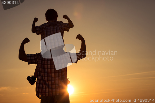 Image of Father and son walking on the field at the sunset time.