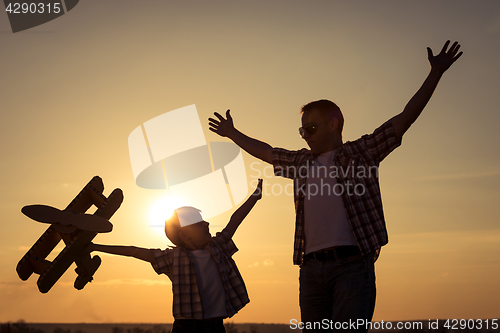 Image of Father and son playing with cardboard toy airplane in the park a