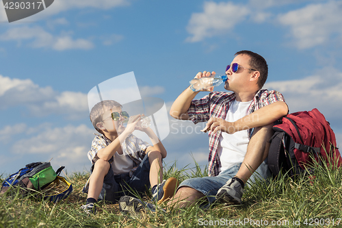 Image of Father and son sitting in the field at the day time.