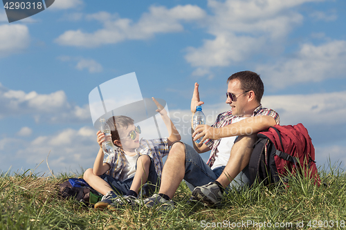 Image of Father and son sitting in the field at the day time.