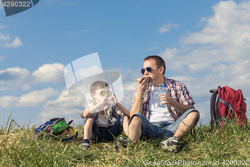 Image of Father and son sitting in the field at the day time.