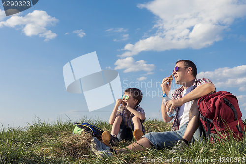 Image of Father and son sitting in the field at the day time.