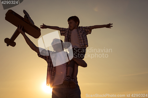 Image of Father and son playing with cardboard toy airplane in the park a