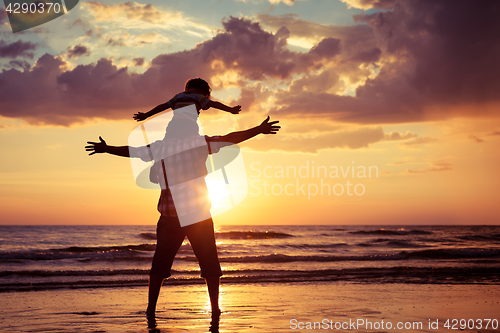 Image of Father and son playing on the beach at the sunset time.