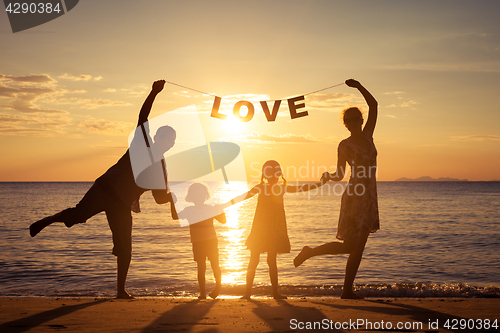 Image of Happy family standing on the beach at the sunset time.