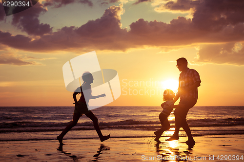 Image of Father and children playing on the beach at the sunset time.