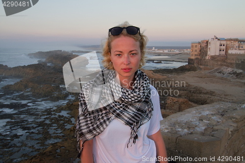 Image of Female traveler standing on city fortress wall of Essaouira, Morocco in sunset.