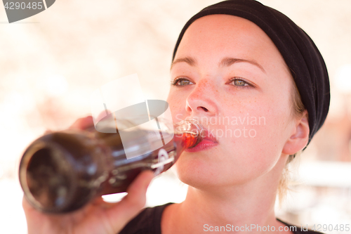 Image of Thirsty active female traveler drinking cola soft dring from glass bottle.