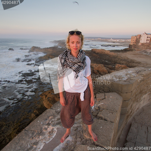 Image of Female traveler standing barefooted on city fortress wall of Essaouira, Morocco.