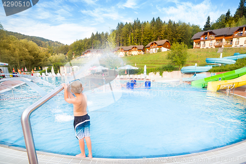 Image of Child playing with water making splashes at the poolside.