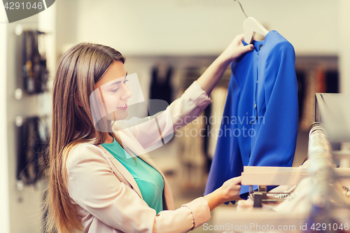 Image of happy young woman choosing clothes in mall