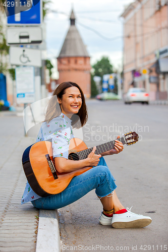 Image of fun smiling woman with a guitar sits on the curb