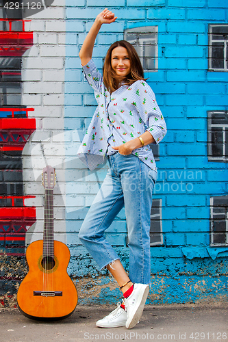 Image of smiling woman in jeans stands near wall with graffiti next to gu