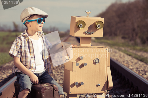 Image of Happy little boy and robot walking with suitcase on the railway 