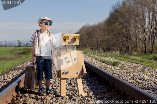 Image of Happy little boy and robot walking with suitcase on the railway 