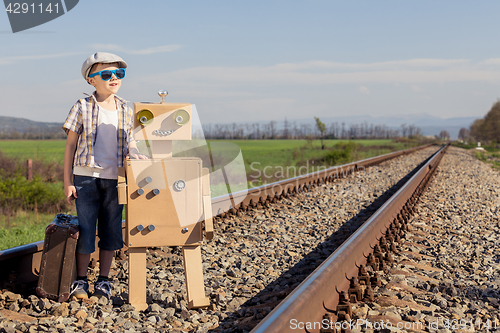 Image of Happy little boy and robot walking with suitcase on the railway 