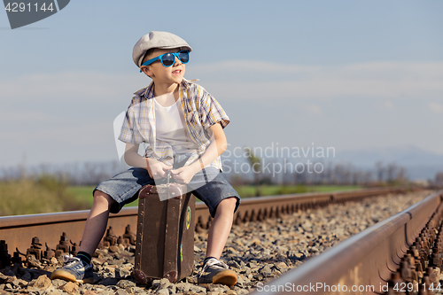 Image of Happy little boy walking with suitcase on the railway at the day