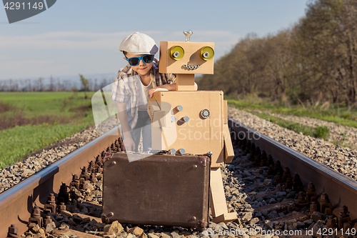 Image of Happy little boy and robot walking with suitcase on the railway 