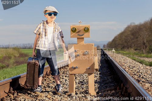 Image of Happy little boy and robot walking with suitcase on the railway 