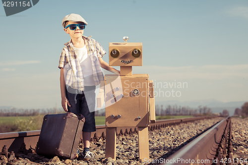 Image of Happy little boy and robot walking with suitcase on the railway 