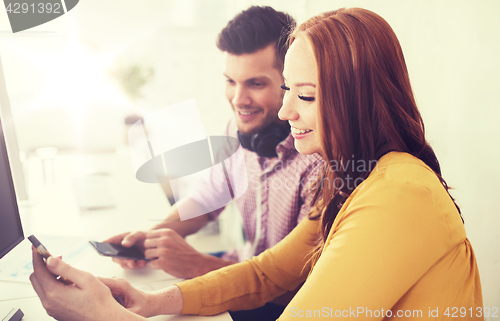 Image of happy creative team with smartphones at office