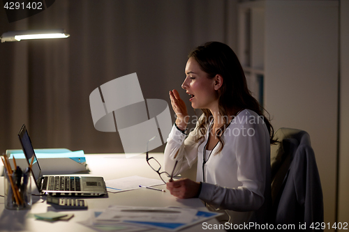 Image of tired woman with laptop yawning at night office